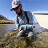 An angler with Navy Gingham Shirt, a wader, and hat catches a fish.