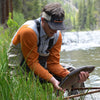 angler wearing a visor, wader and a gray shirt, while catching a fish 