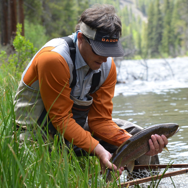 angler wearing a visor, wader and a gray shirt, while catching a fish 