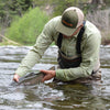 Man wearing complete fishing apparel, catching a fish from water.