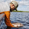Taylor McDaniel is catching a fish in fishing attire i.e. gray and orange shirt, hat, and glasses