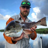 Angler posing with a catch in hand and with frost gray shirt, fishing hat, and sun glasses.