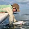 A woman in seaweed shirt and brown fishing hat is catching a fish from boat.